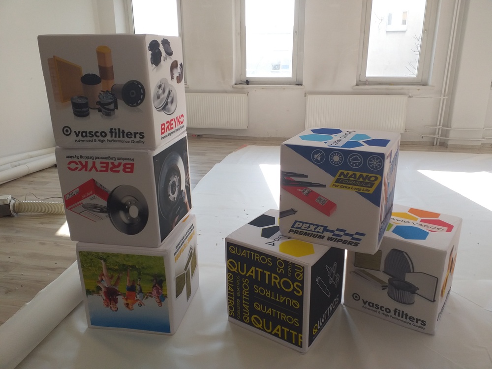 Zestaw kilku puf w kształcie kostek z logotypami marek motoryzacyjnych, takich jak Vasco Filters, Breyko i Pexa.