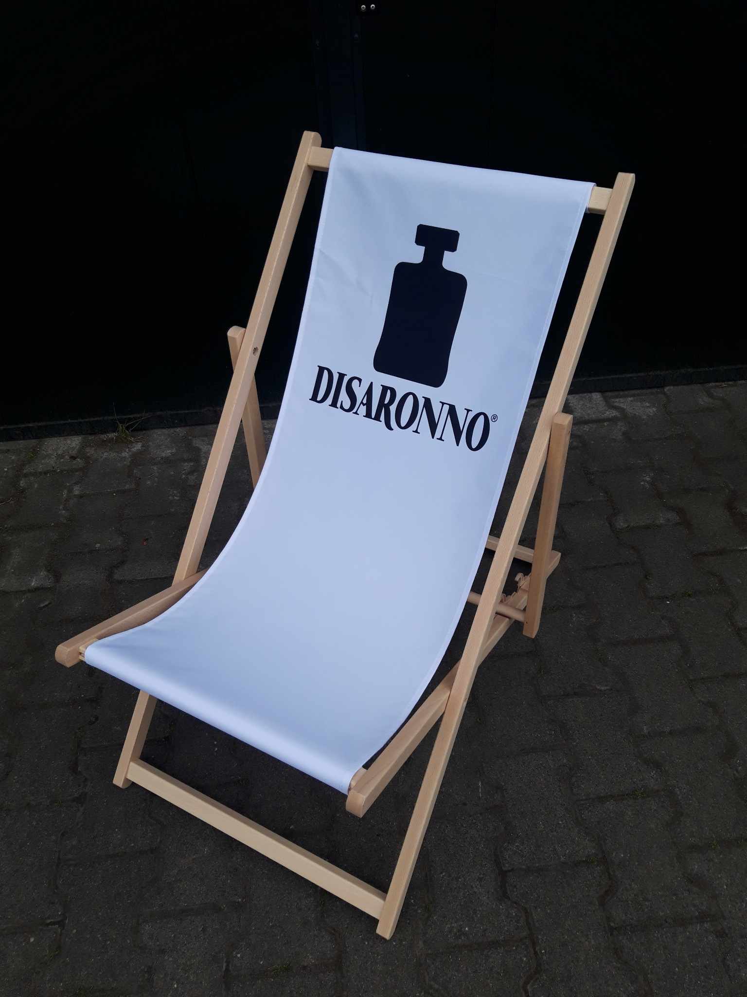 Drewniany leżak plażowy z białym siedziskiem, na którym widnieje czarne logo marki Disaronno oraz ikona charakterystycznej butelki.