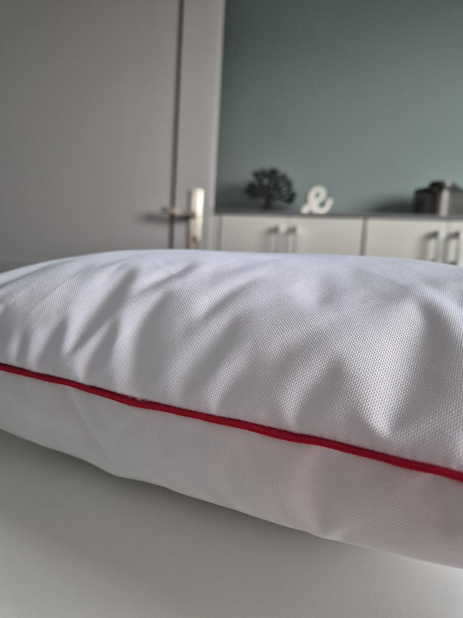 Zbliżenie na białą poduszkę reklamową z czerwoną lamówką, pokazujące strukturę tkaniny.