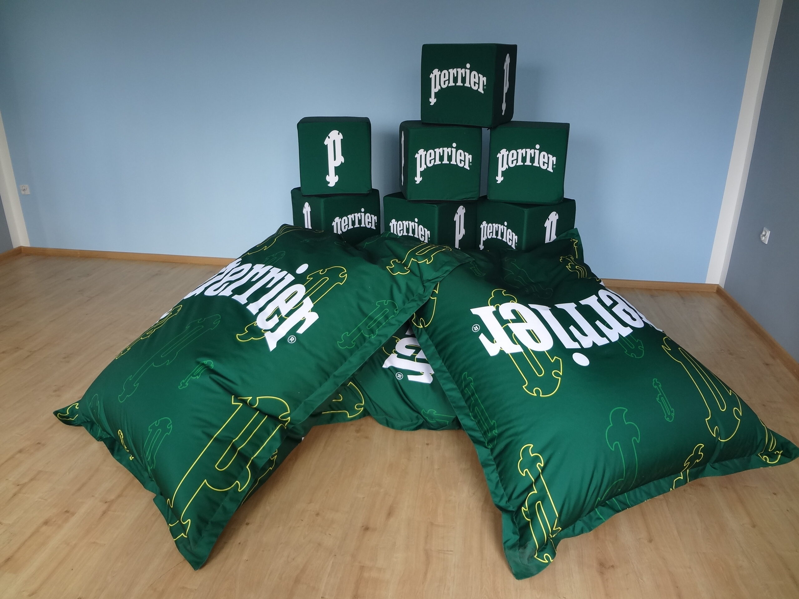 Aranżacja mebli reklamowych marki Perrier obejmująca duże pufy typu „bean bag” oraz stos kostek z logotypem.