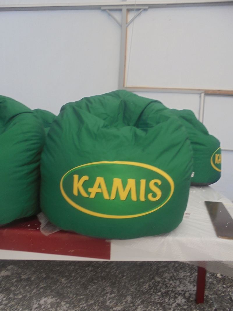 Zielona pufa reklamowa typu „bean bag” z wyraźnym żółtym logotypem marki Kamis wpisanym w owal.
