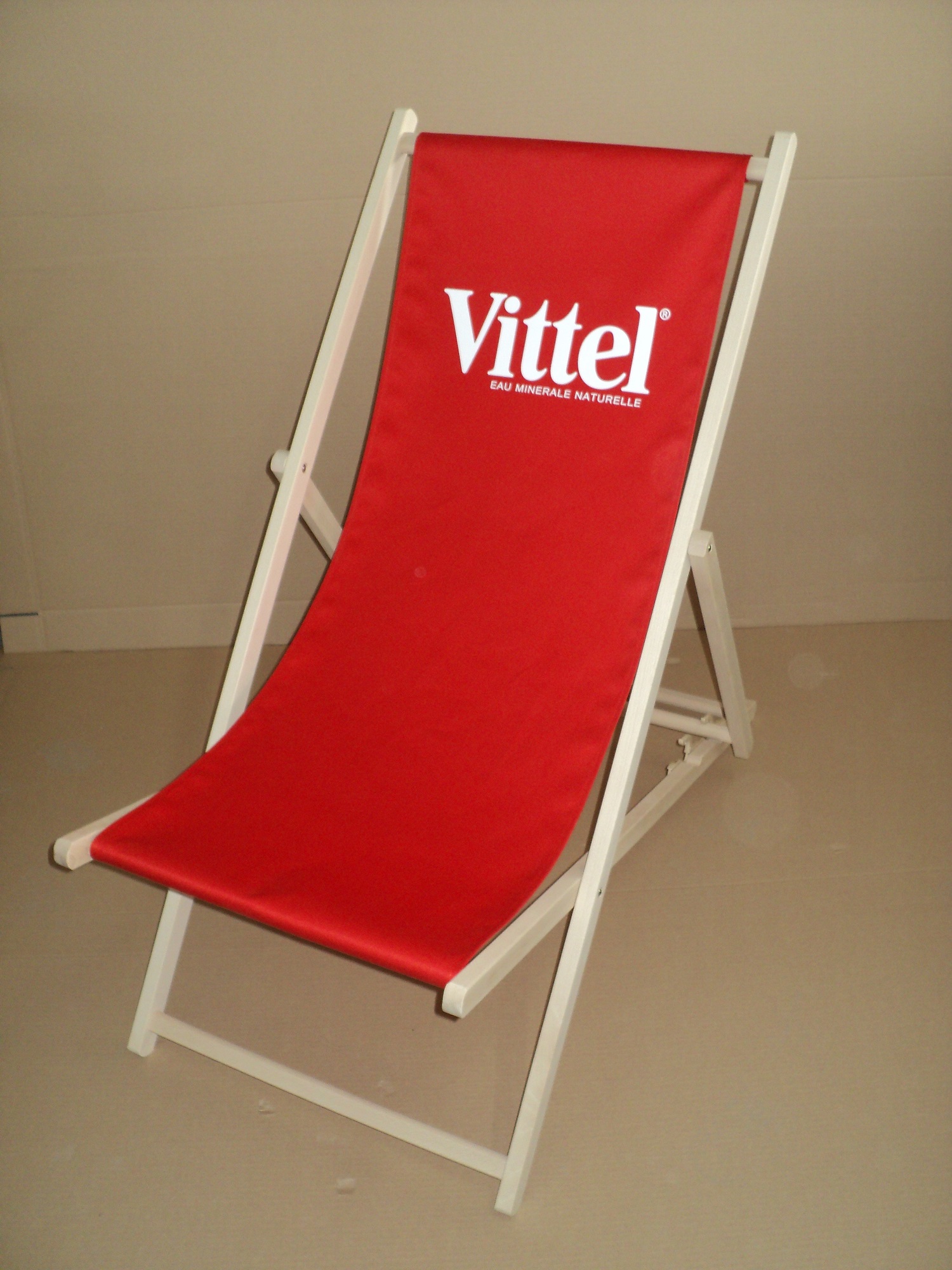 Czerwony leżak plażowy z białym logotypem marki wody mineralnej Vittel na siedzisku.
