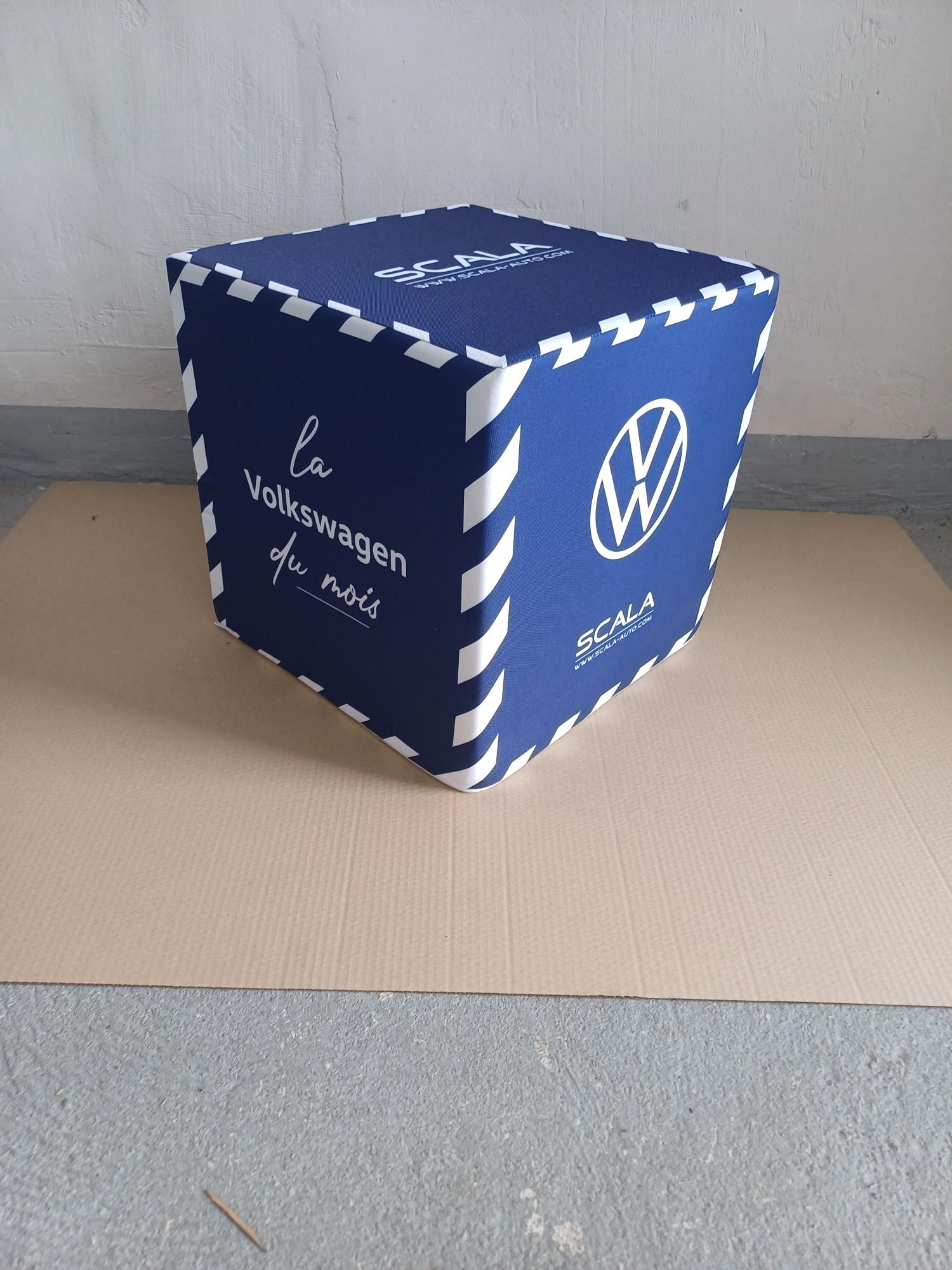 Granatowa pufa reklamowa w kształcie kostki z logotypami Volkswagen i Scala oraz napisem "la Volkswagen du mois".
